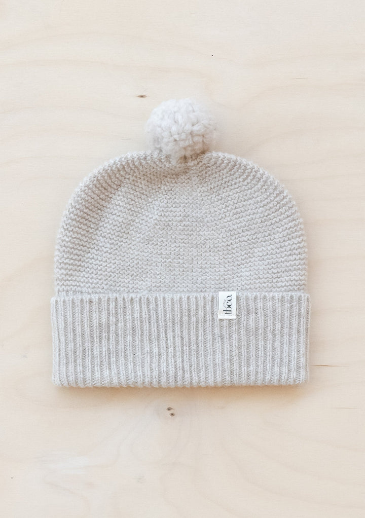 TBCo Merino Wool Baby Beanie in oatmeal melange with white pom-pom, knitted ribbed hem and small brand label