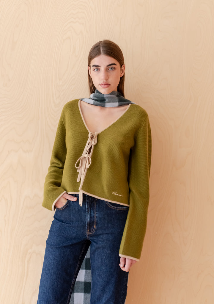 Model wearing TBCo Merino Wool Tie Cardigan in Green with oatmeal edging and tie closures over jeans.
