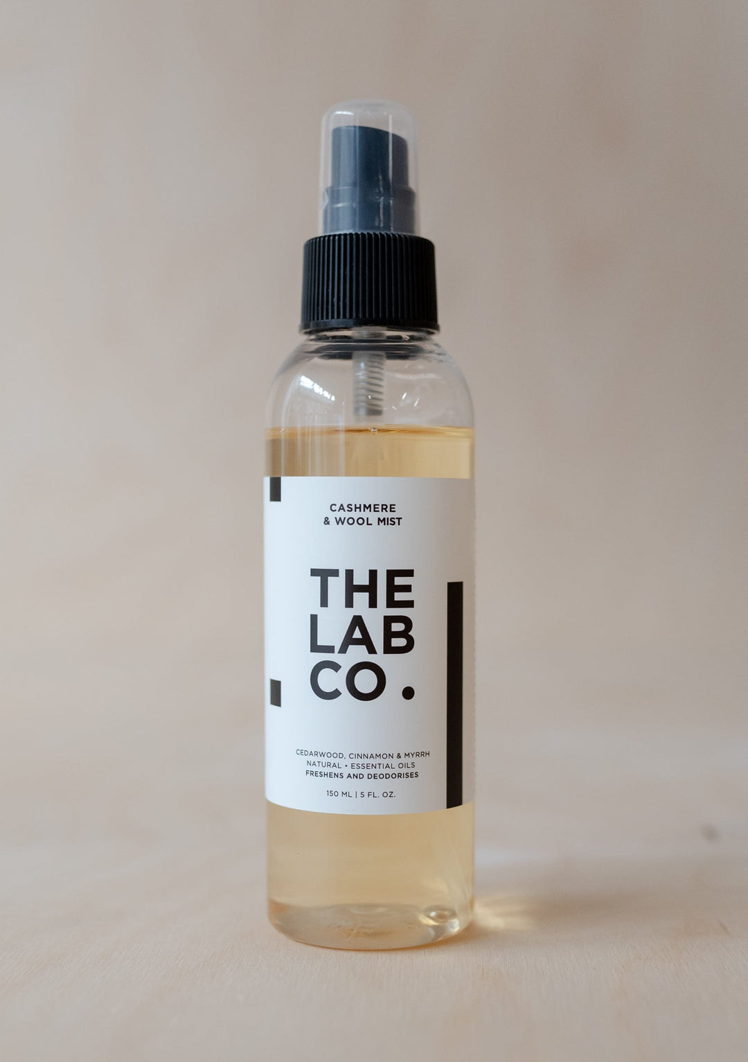 TBCo Cashmere & Wool Mist bottle with black spray nozzle, clear glass design showing amber-tinted liquid, minimalist labelling