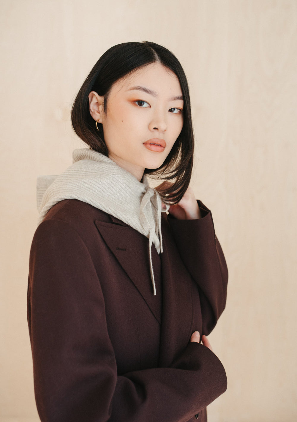 TBCo Merino Hood in Oatmeal Melange worn with brown coat, showcasing soft wool texture and versatile winter styling