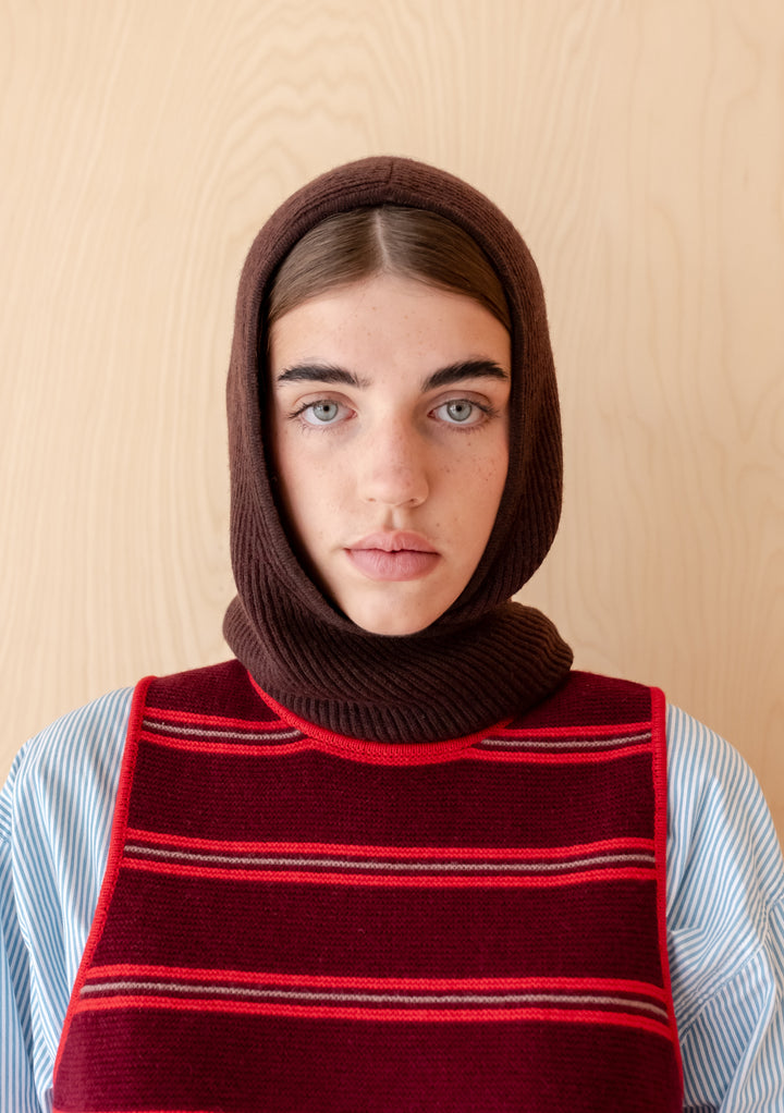 Woman wearing TBCo Merino Hood in Brown Two-Tone styled over a striped shirt and red vest against a wooden background