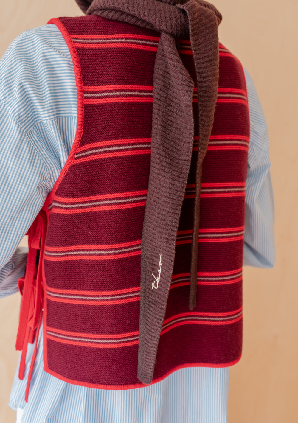 Person wearing TBCo Merino Hood in Brown Two-Tone with long ties over a red striped vest and blue shirt