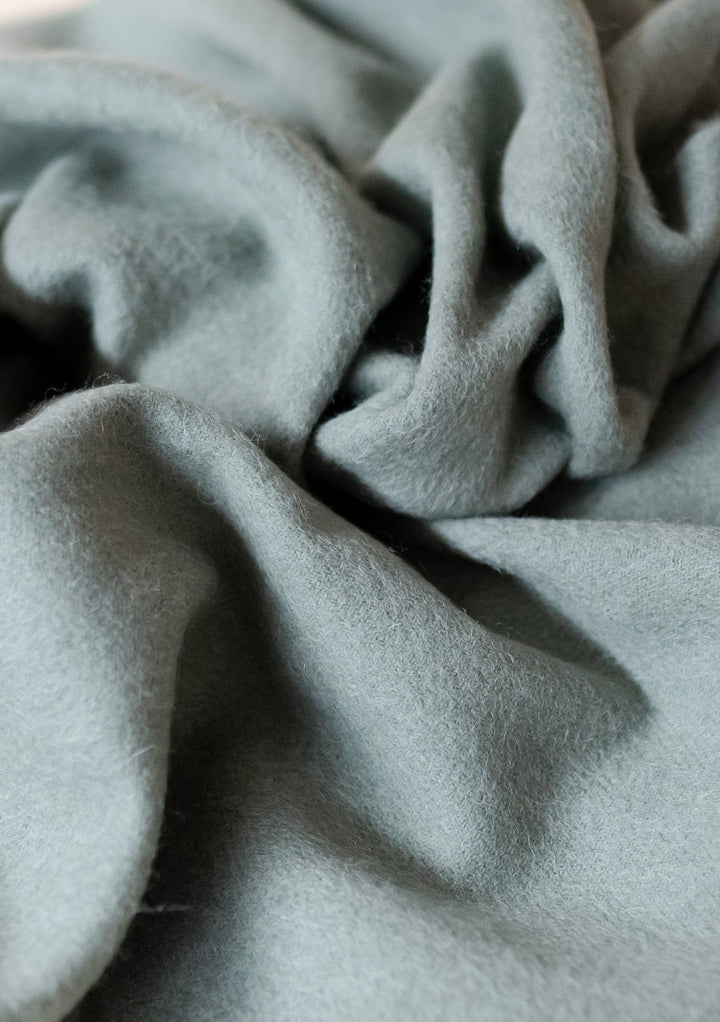 Close-up texture of TBCo Men's Lambswool Scarf in Sage Melange showing soft, draped wool fabric with gentle folds
