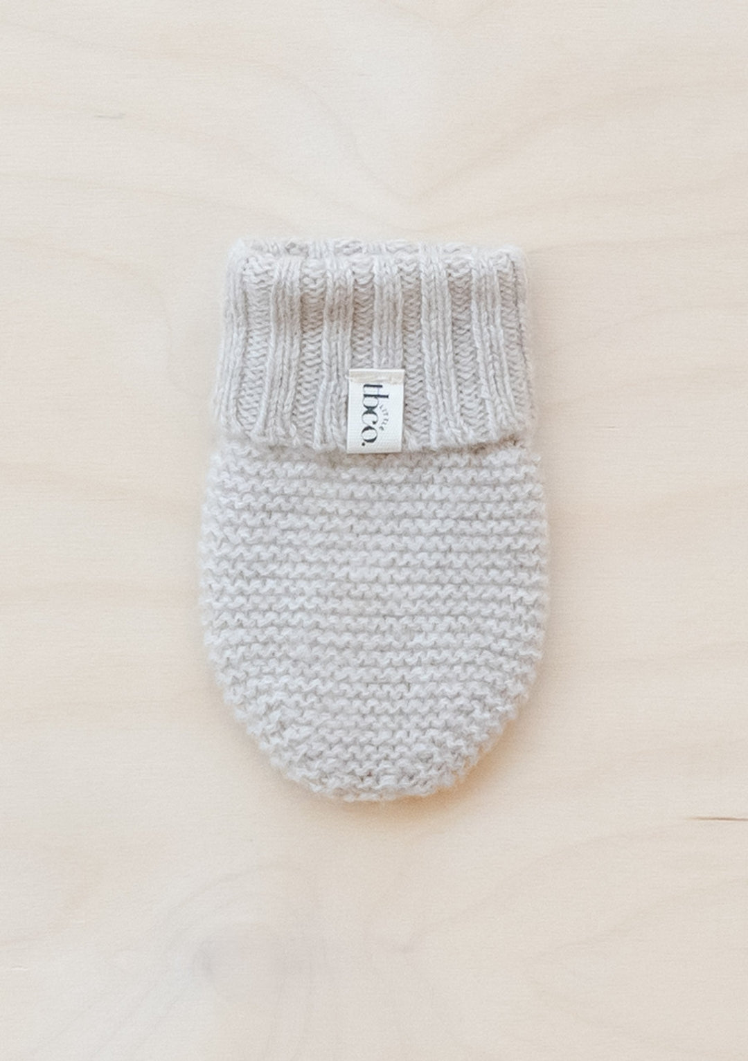TBCo Merino Wool Baby Mittens in Oatmeal Melange knitted with ribbed cuff and label, displayed on cream background
