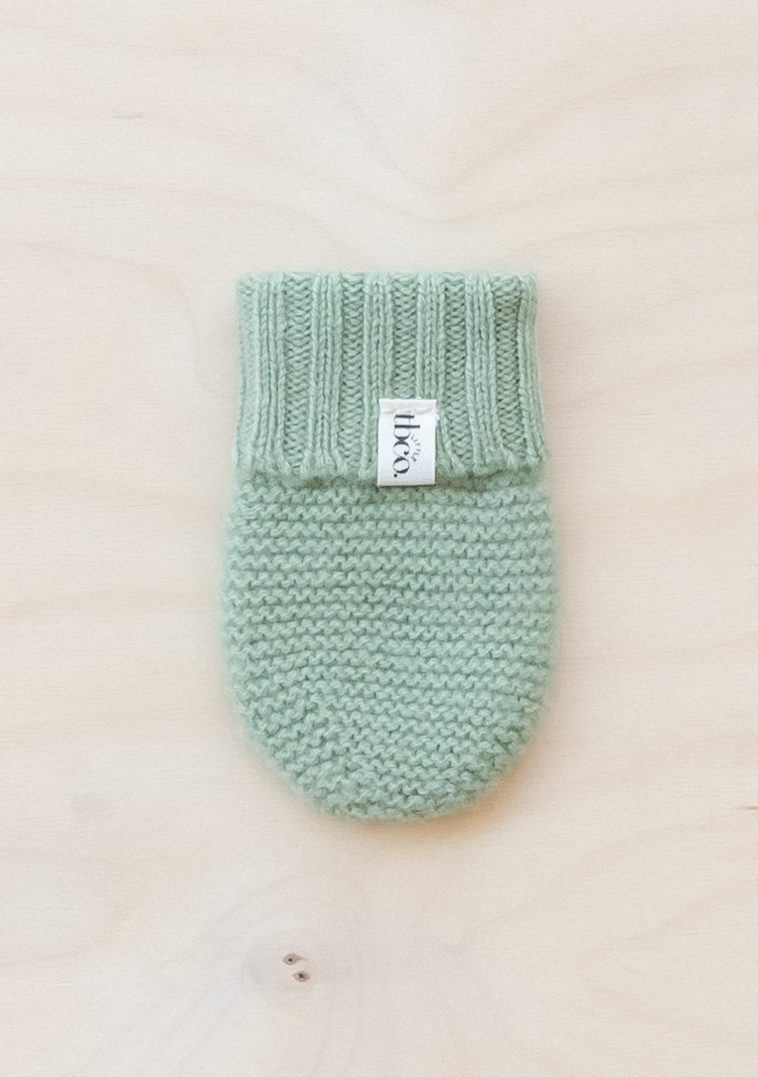 TBCo Merino Wool Baby Mittens in soft pistachio green, knitted with ribbed cuff detail and brand label