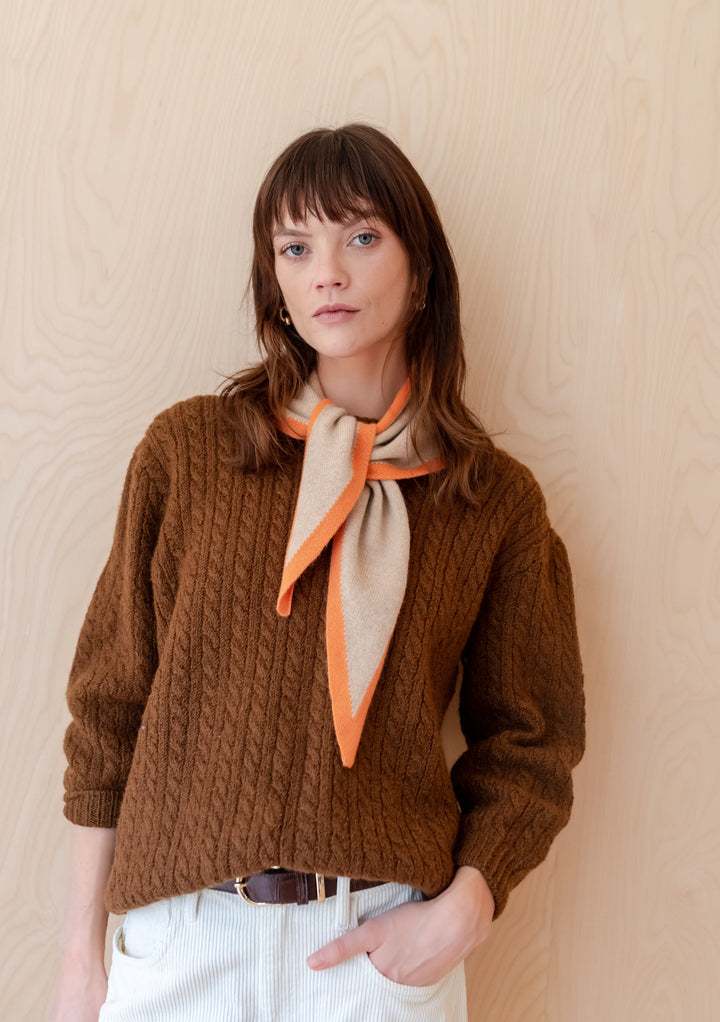 TBCo Merino Triangle Scarf in camel and apricot styled with brown cable knit jumper against wooden backdrop