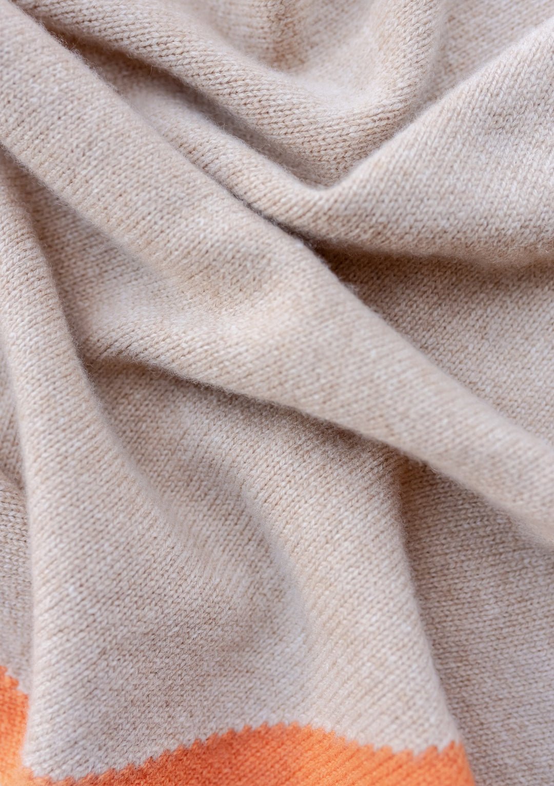 Close-up texture detail of TBCo Merino Triangle Scarf in camel with apricot edge, showing soft knitted wool fabric