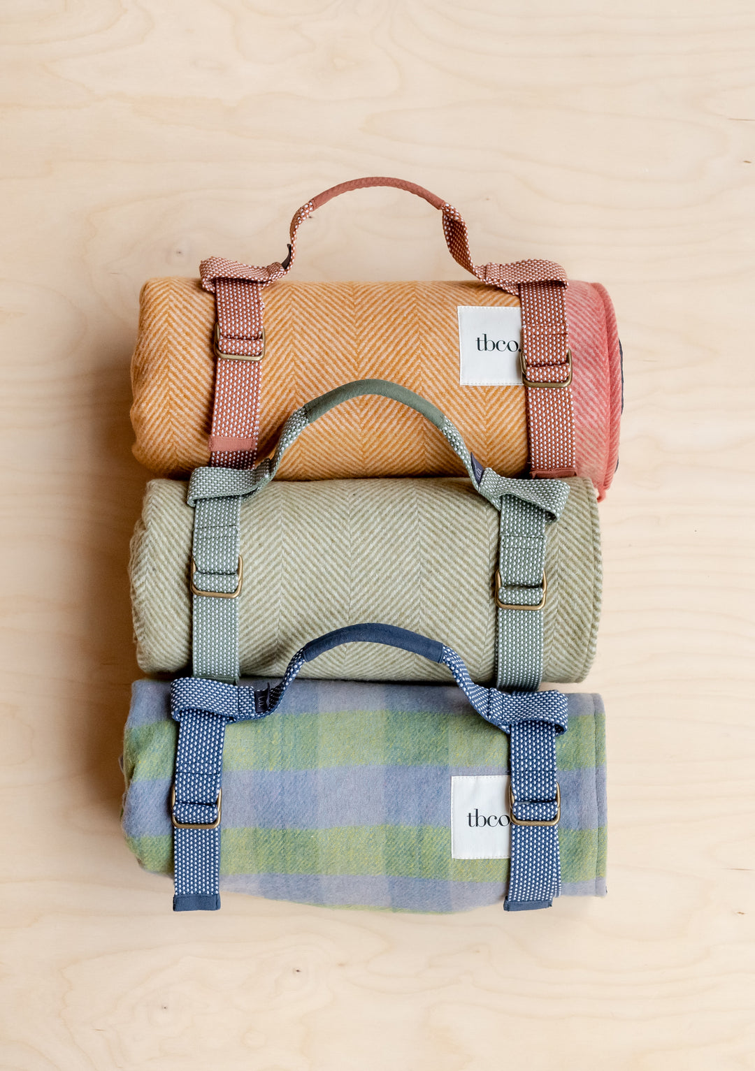 3 TBCo picnic blankets rolled up in recycled plastic picnic carriers.