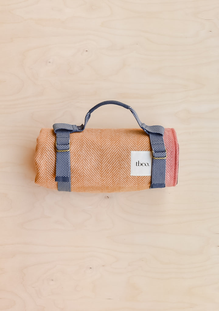 A TBCo recycled wool picnic blanket in mustard frame check, rolled up and held in a recycled plastic TBCo picnic carrier.