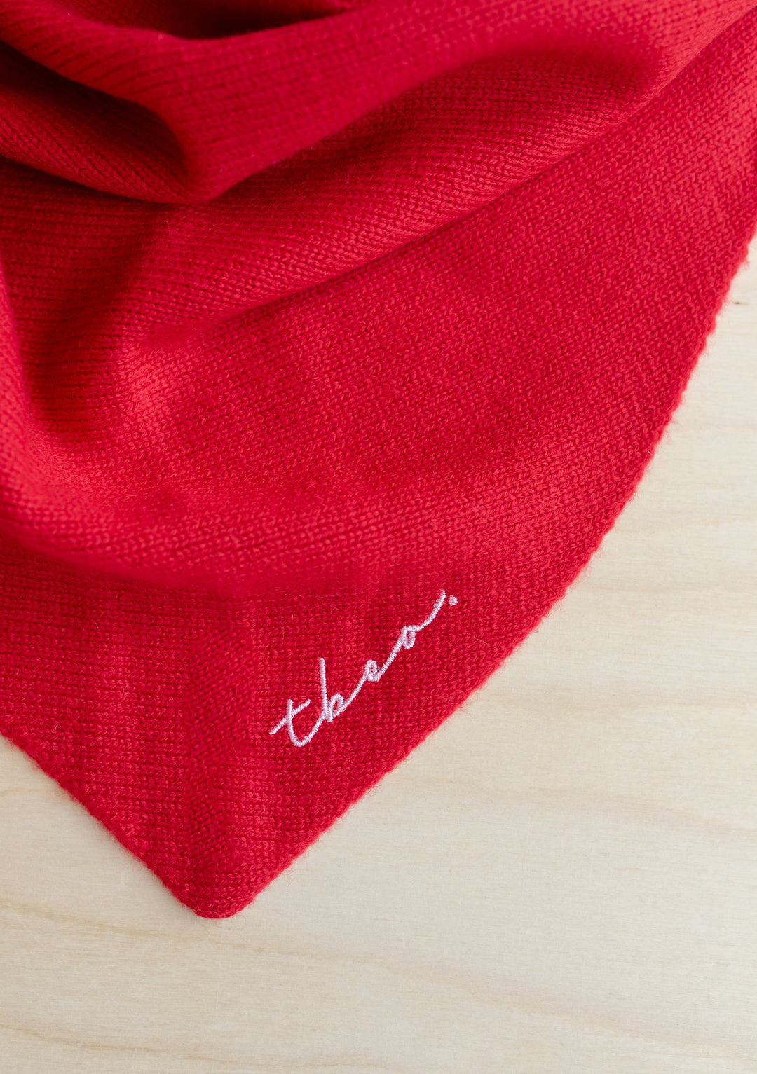 Red merino wool triangle scarf by TBCo featuring lilac embroidered logo, showcasing soft knit texture and versatile styling options