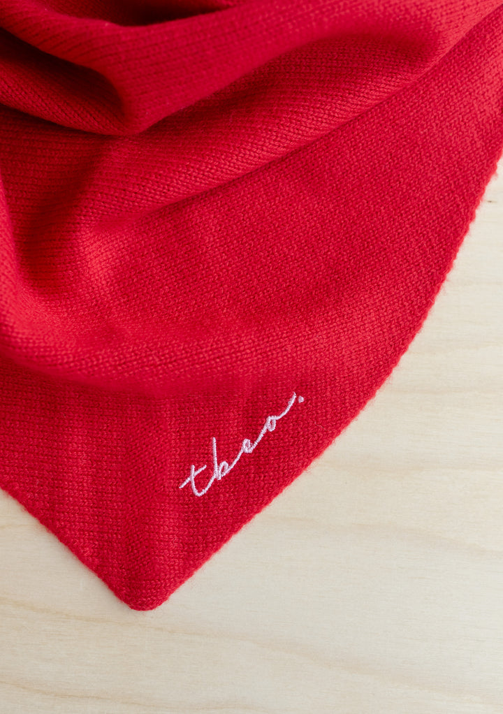 Red merino wool triangle scarf by TBCo featuring lilac embroidered logo, showcasing soft knit texture and versatile styling options