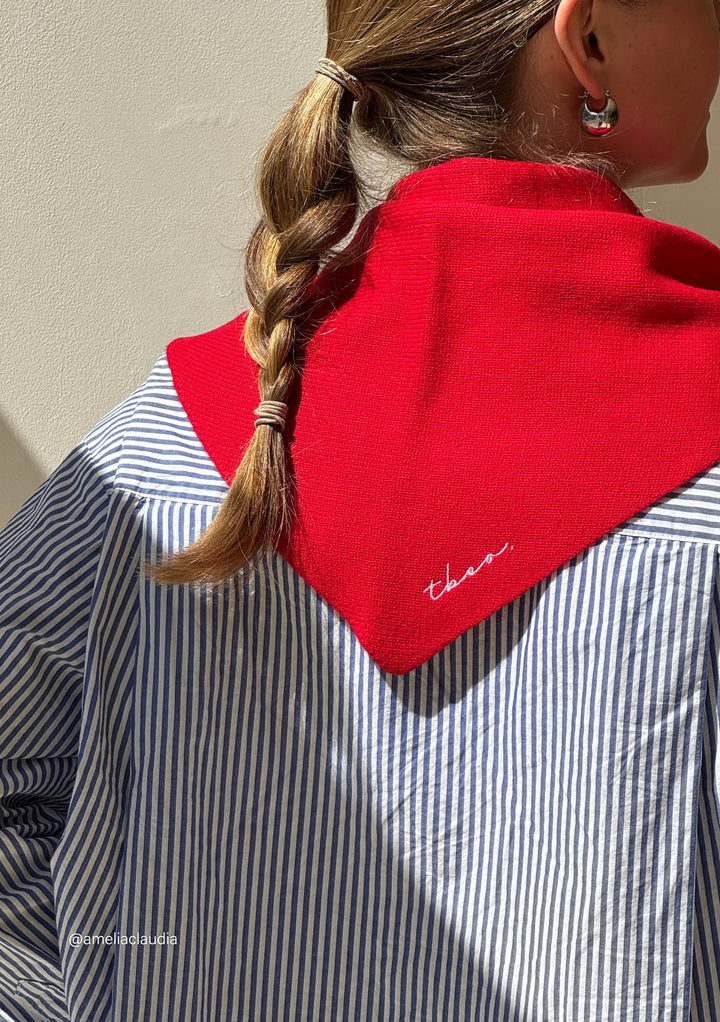 Woman wearing TBCo Merino Triangle Scarf in Red over striped shirt, embroidered logo visible on soft merino wool fabric