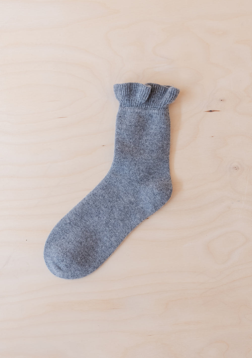 Single Merino Wool Socks in Charcoal Frilly by TBCo laid flat on light wood background with ruffled edge detail
