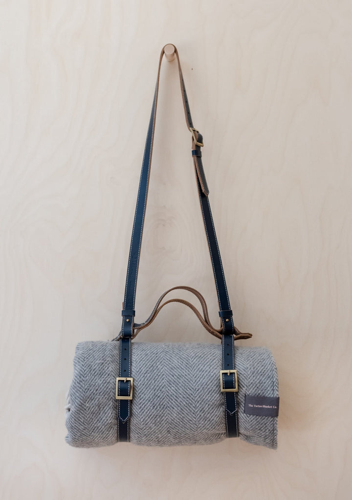 TBCo Leather Picnic Carrier with adjustable shoulder strap and brass buckles holding grey wool blanket against white background