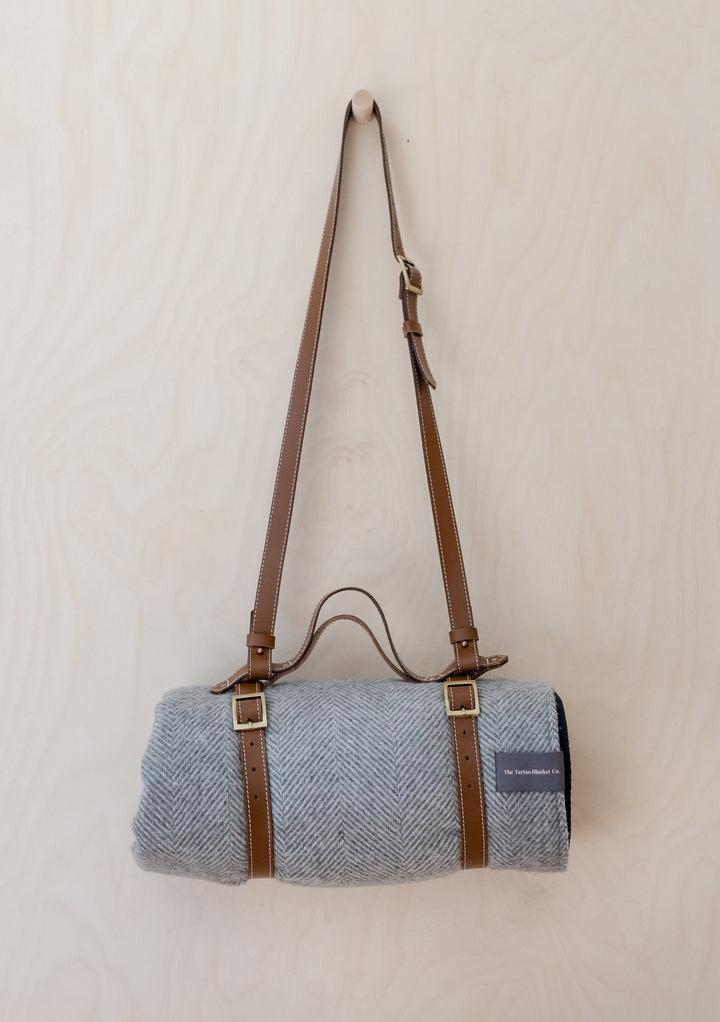 TBCo leather picnic carrier with adjustable shoulder strap shown with grey wool blanket and brass buckle details