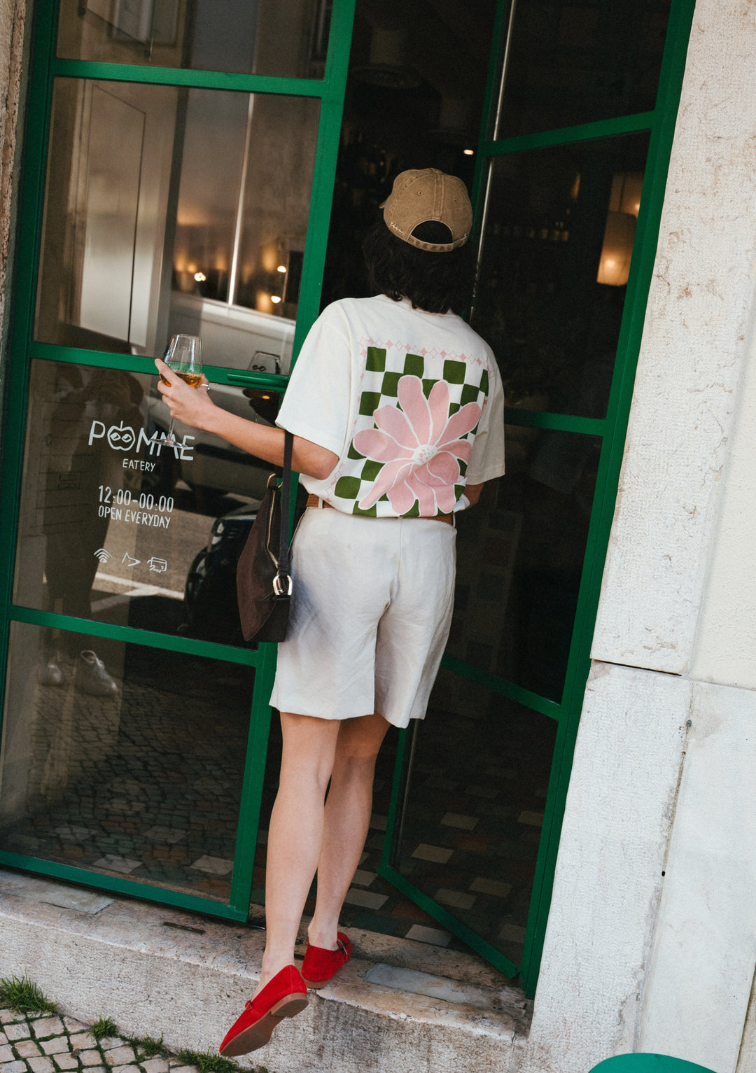 TBCo Cotton T-Shirt in Ecru Flora featuring pink and green floral checkerboard design shown at cafe entrance