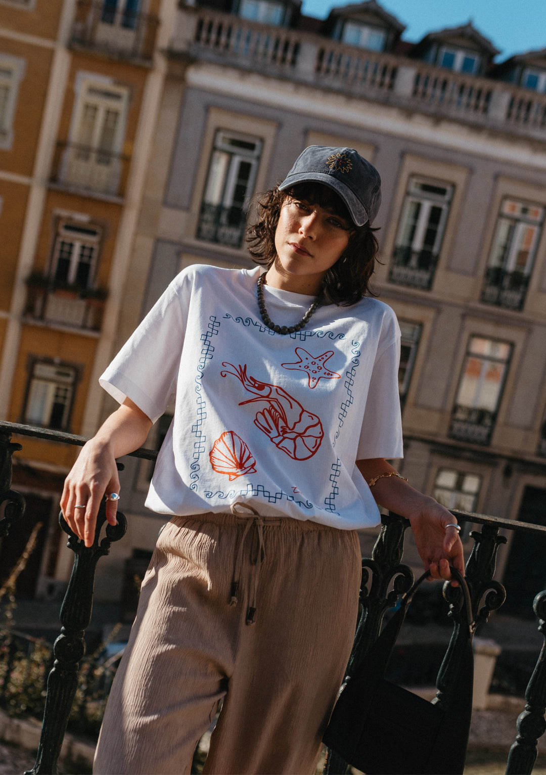 TBCo Cotton T-Shirt in White Shrimp with red sea creature illustrations and blue border pattern styled against urban architecture