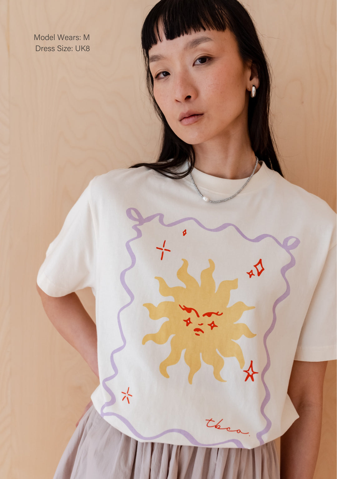 Cream cotton t-shirt by TBCo featuring yellow sun illustration with lilac border and red stars, displayed on minimalist background