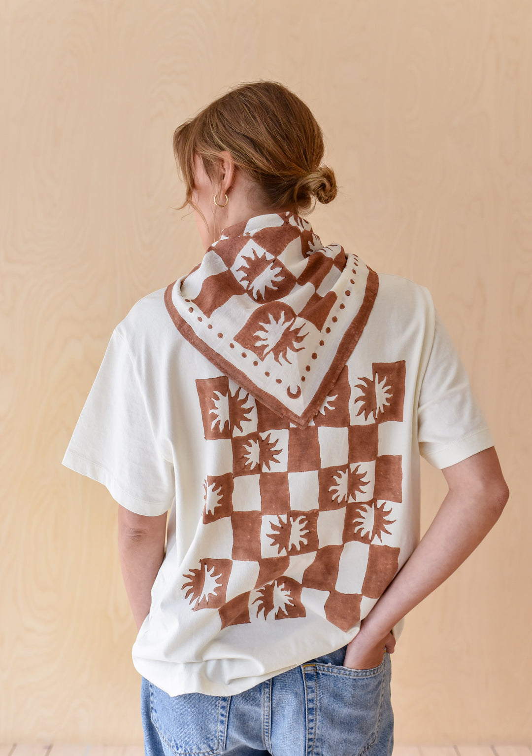 Person wearing The Artist Series TBCo x Frankie Penwill Cotton T-Shirt with sunburst checkerboard pattern, matching neckerchief, and relaxed-fit jeans, viewed from behind.
