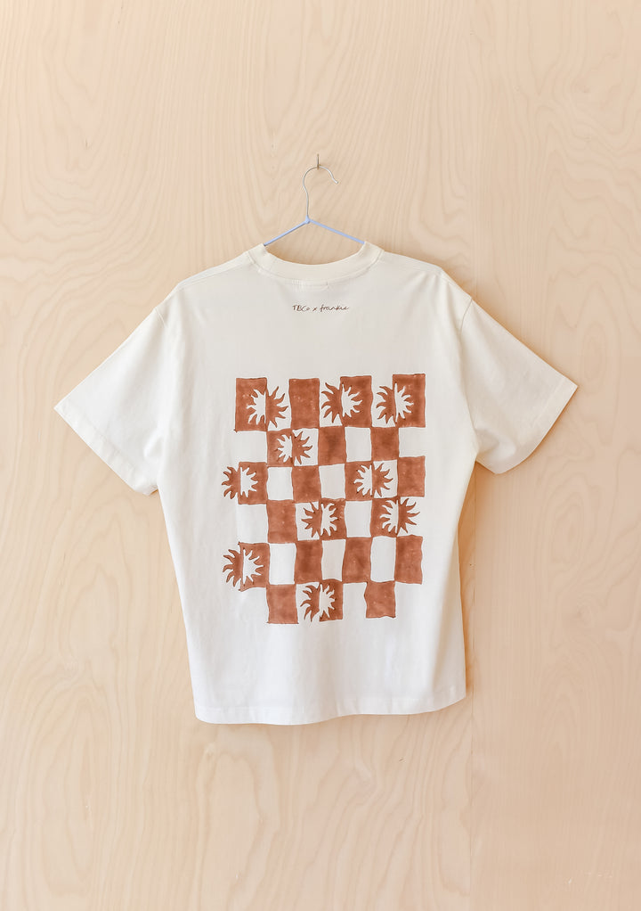 The Artist Series TBCo x Frankie Penwill Cotton T-Shirt features a grid of rust-brown squares with sunburst patterns, showcasing unique artistry on a white background.