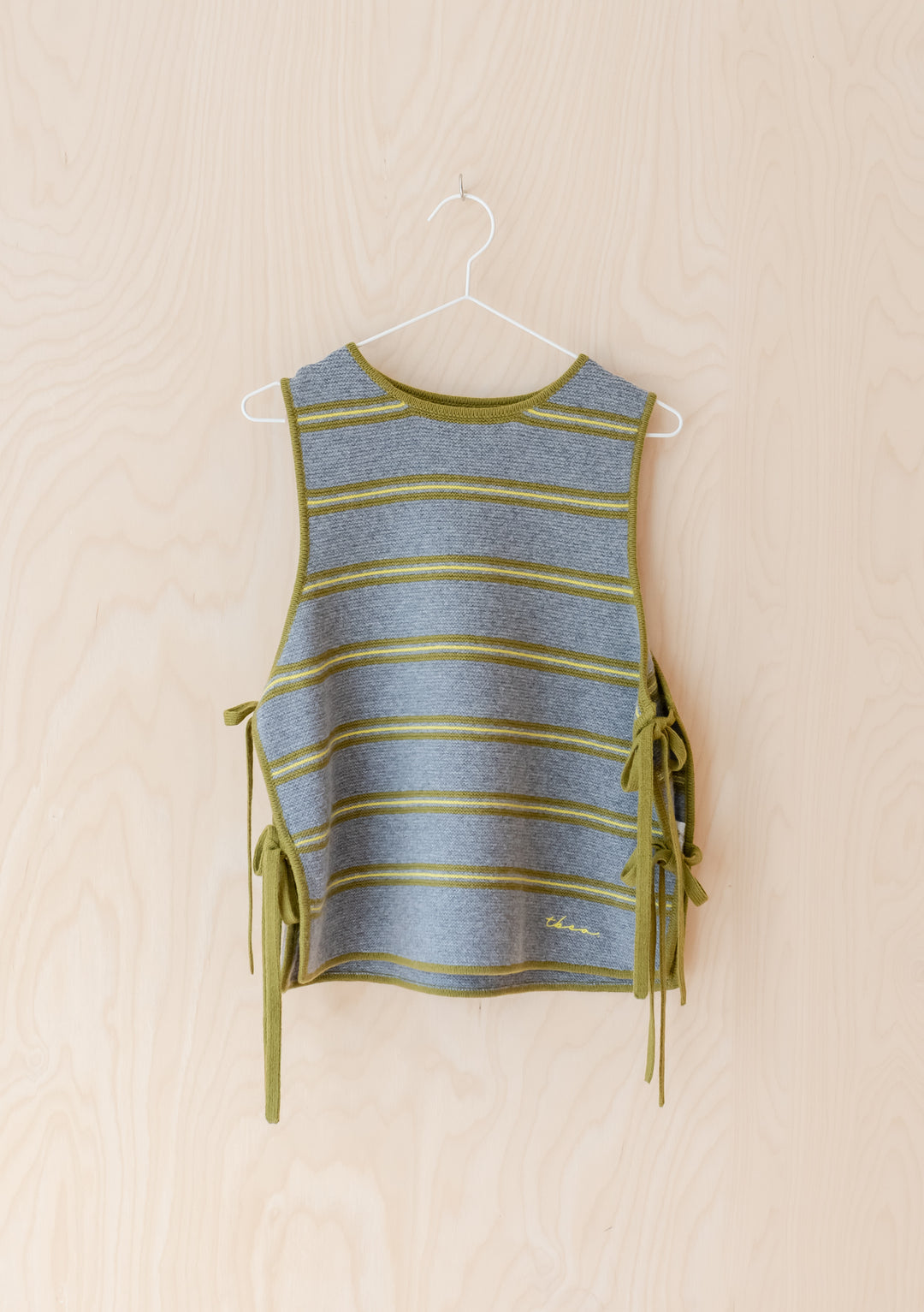 Merino Wool Tie Vest in Green Stripe by TBCo hanging on wooden background with adjustable side ties and embroidered logo