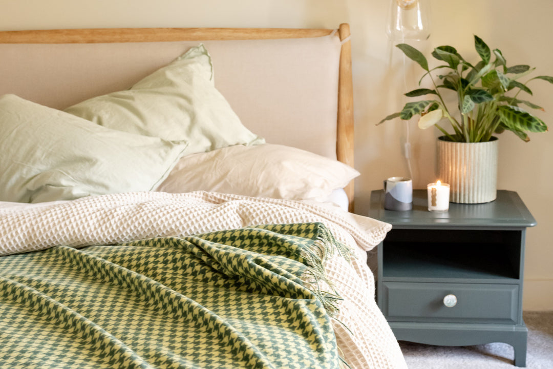 A bedroom scene with one of TBCo's lambswool green houndstooth blankets draped over the bed.