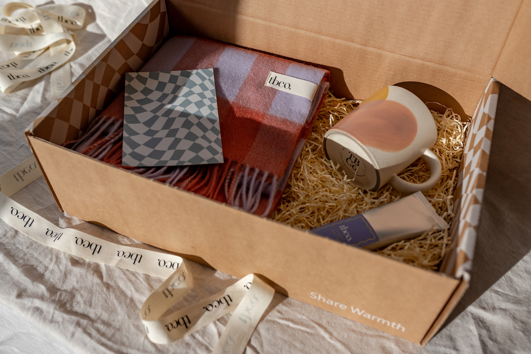 A Mother's Day gift box containing TBCo gingham scarf, mug, hand cream and gift note.