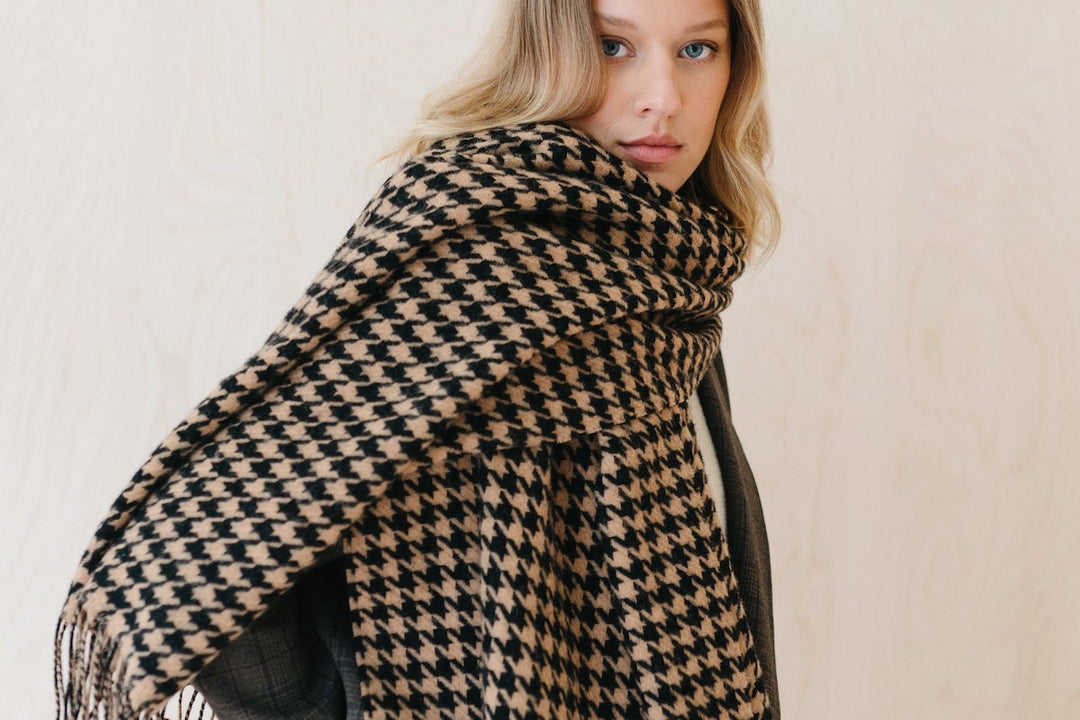 Model wearing a TBCo lambswool scarf in a camel brown and black houndstooth pattern.