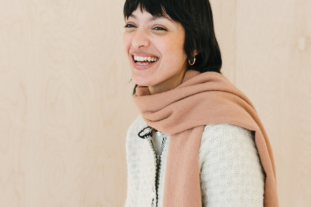 A model laughing wearing a TBCo blush pink cashmere scarf.