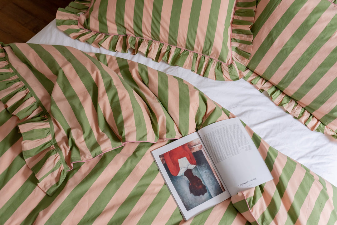 TBCo Bedding - An unmade bed, featuring TBCo's green stripe duvet cover and pillowcases, with an open magazine laid on top.