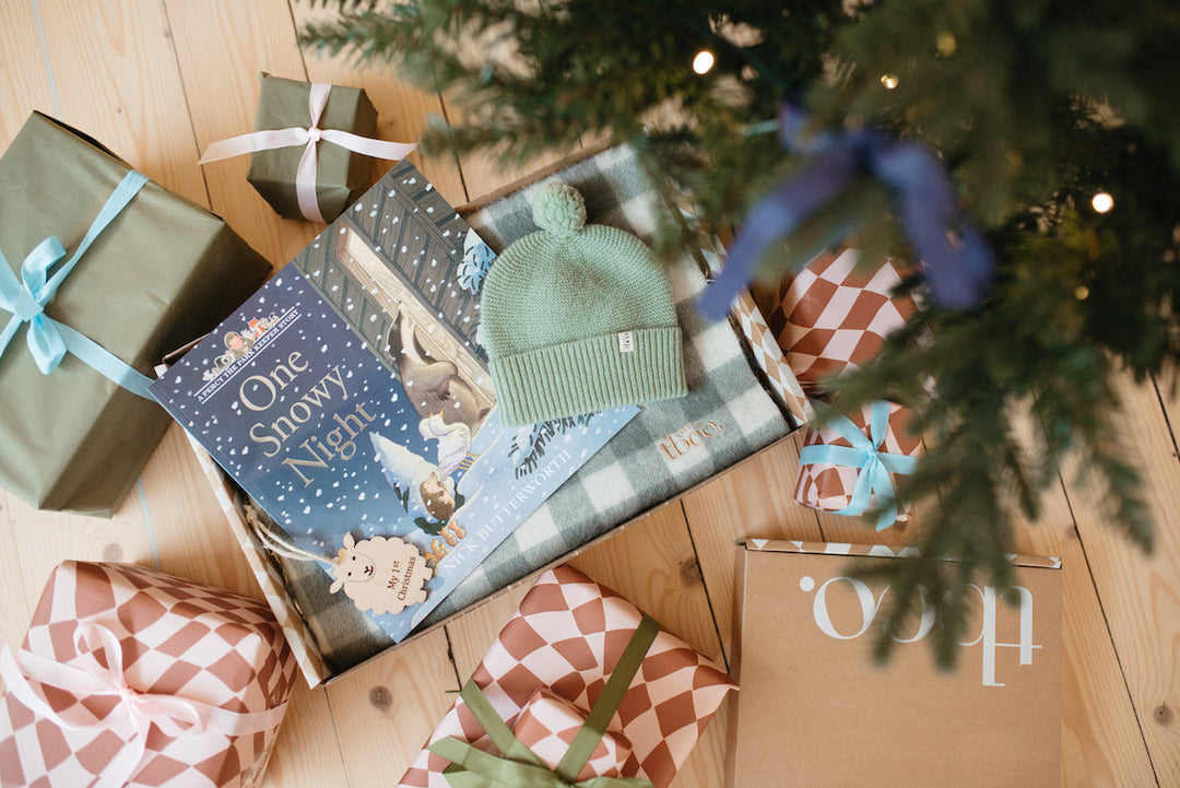 A gift box for a newborn baby, including a TBCo green gingham baby blanket, sage green beanie hat and baby book.