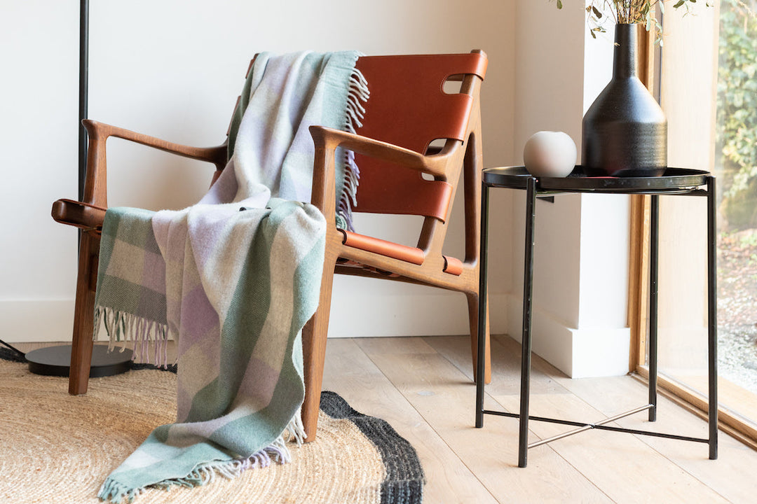 A TBCo checked blue and lilac lambswool blankets draped over a brown leather chair.