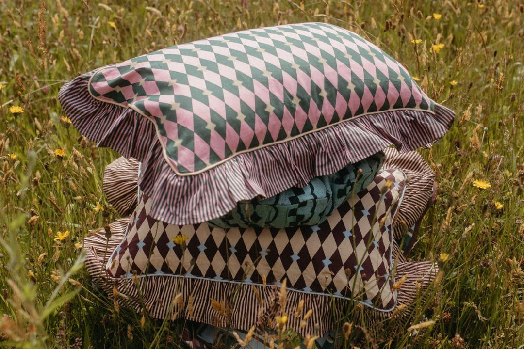 A bedroom scene with TBCo cotton green throw and pink frilled cushions scattered across a bed with a breakfast tray laid on top.