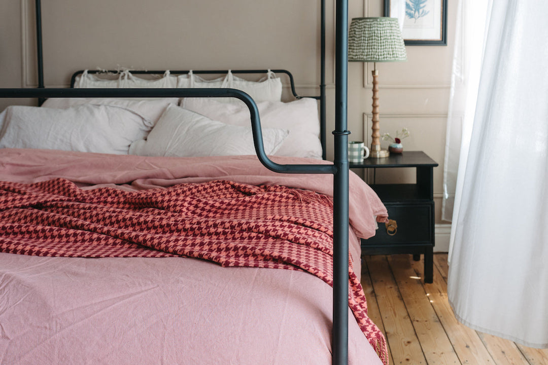 A four poster bed with a TBCo pink houndstooth lambswool blanket draped across it.