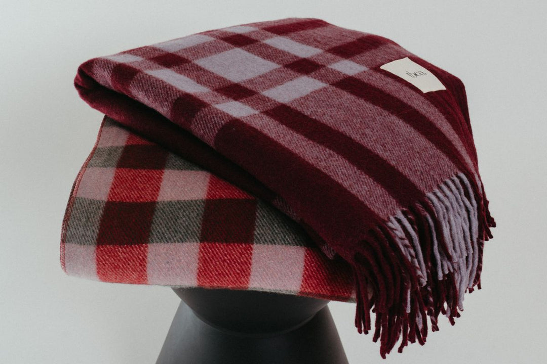 A TBCo recycled wool block check blanket draped across a purple sofa.