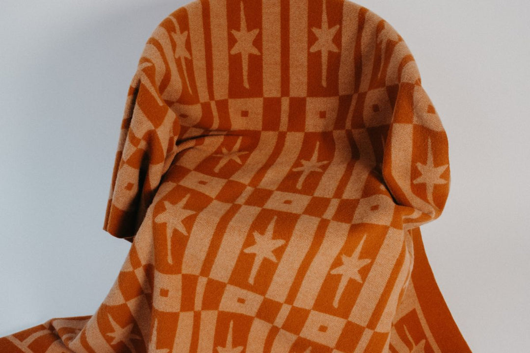 A TBCo lambswool blanket in multicoloured check draped across a four poster bed.