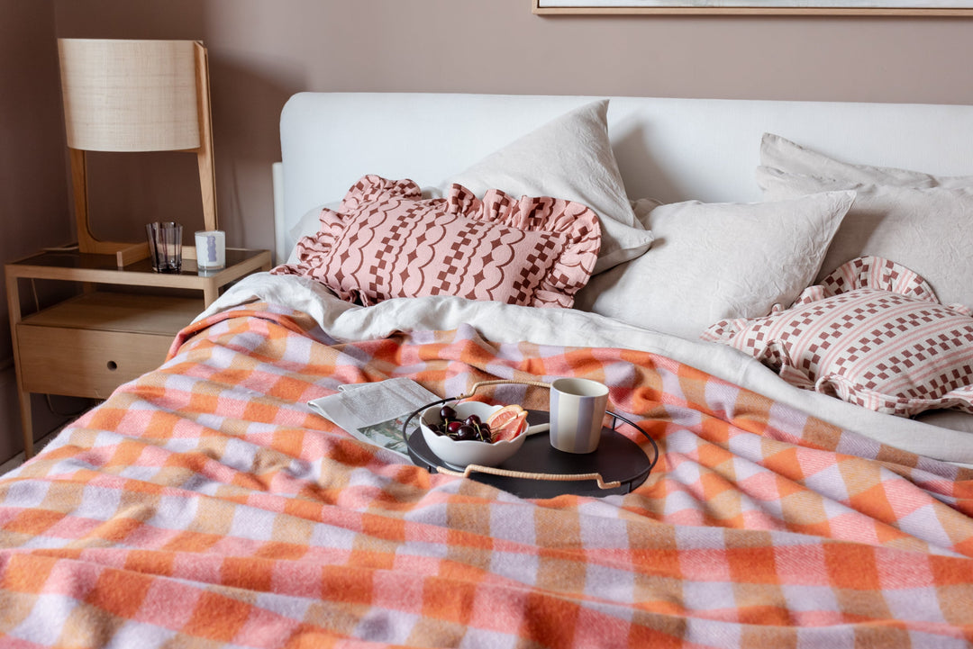 Bedroom scene with TBCo orange gingham blanket and two pink frilled cushions scattered on the bed.