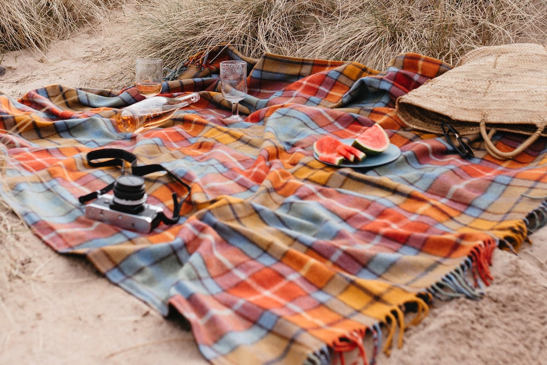 A TBCo green and blue check picnic blanket laid out on a sandy beach.