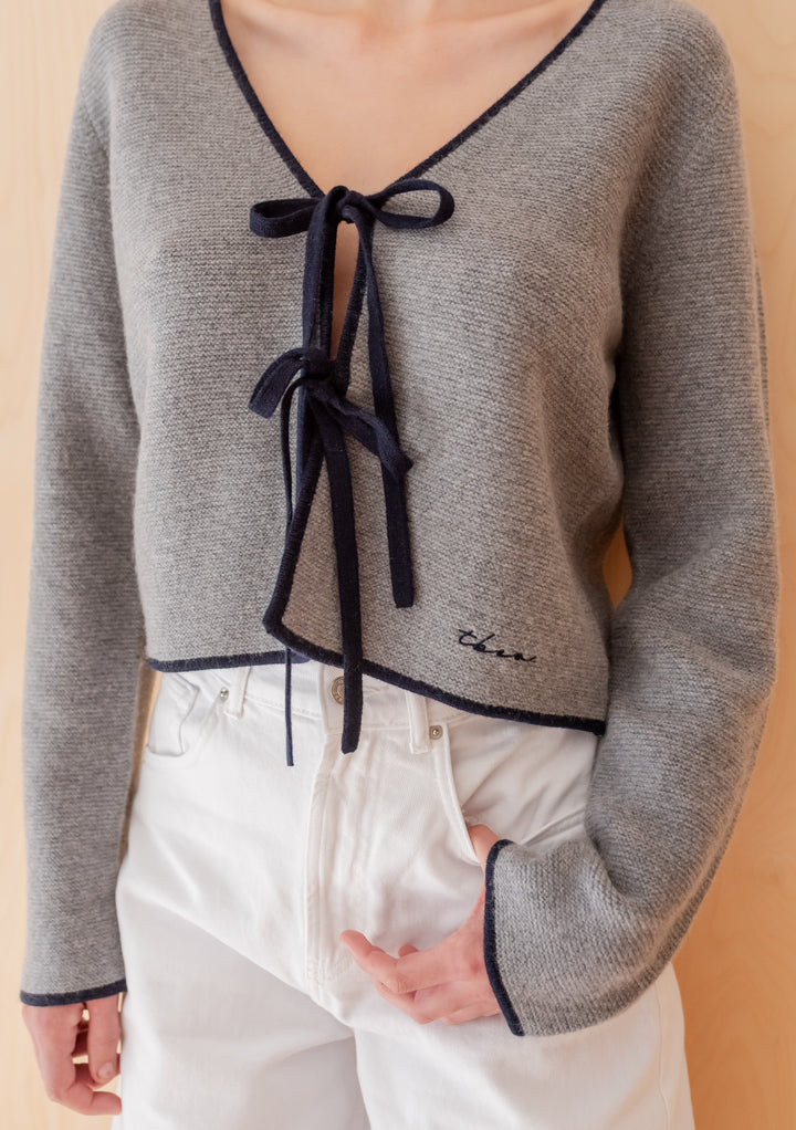 TBCo Merino Wool Tie Cardigan in Grey, featuring a deep V-neck with navy ribbon ties and trims, styled with high-waisted jeans for an elegant, versatile look.