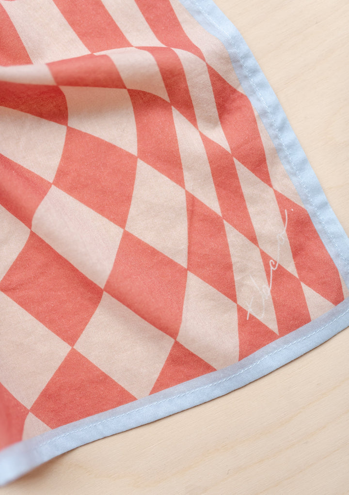 Close-up of TBCo Sample Sale Cotton Square Scarf in Apricot Checkerboard showing soft fabric and pale blue border on light surface
