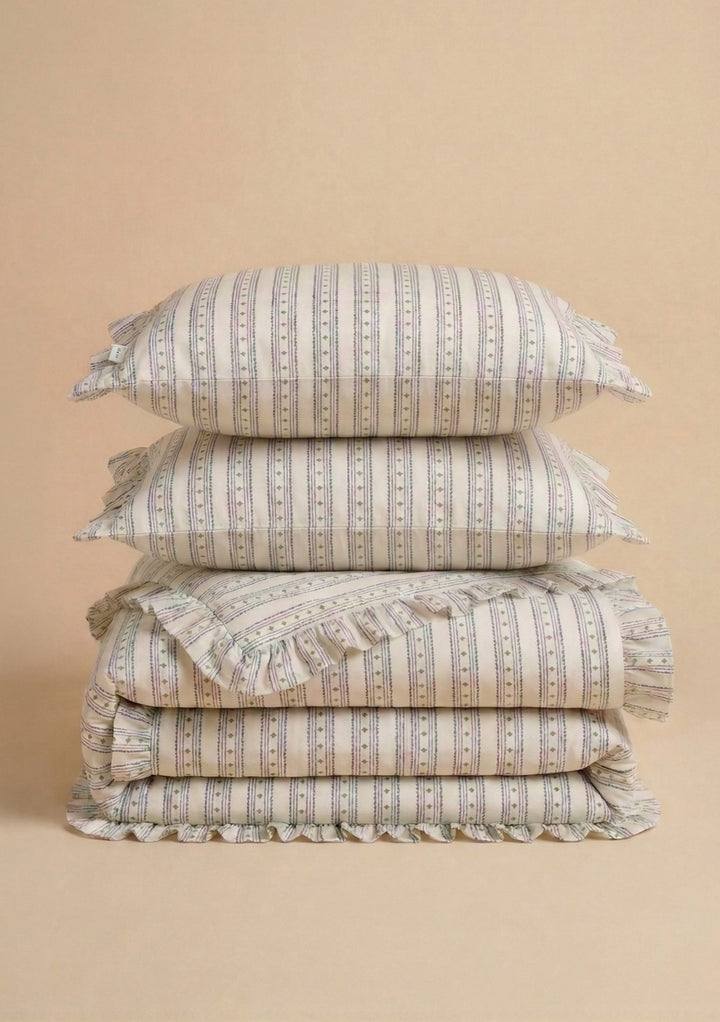 Pair of Cotton Pillowcases in Navy Ditsy Floral by TBCo stacked with matching cotton bedding on beige background
