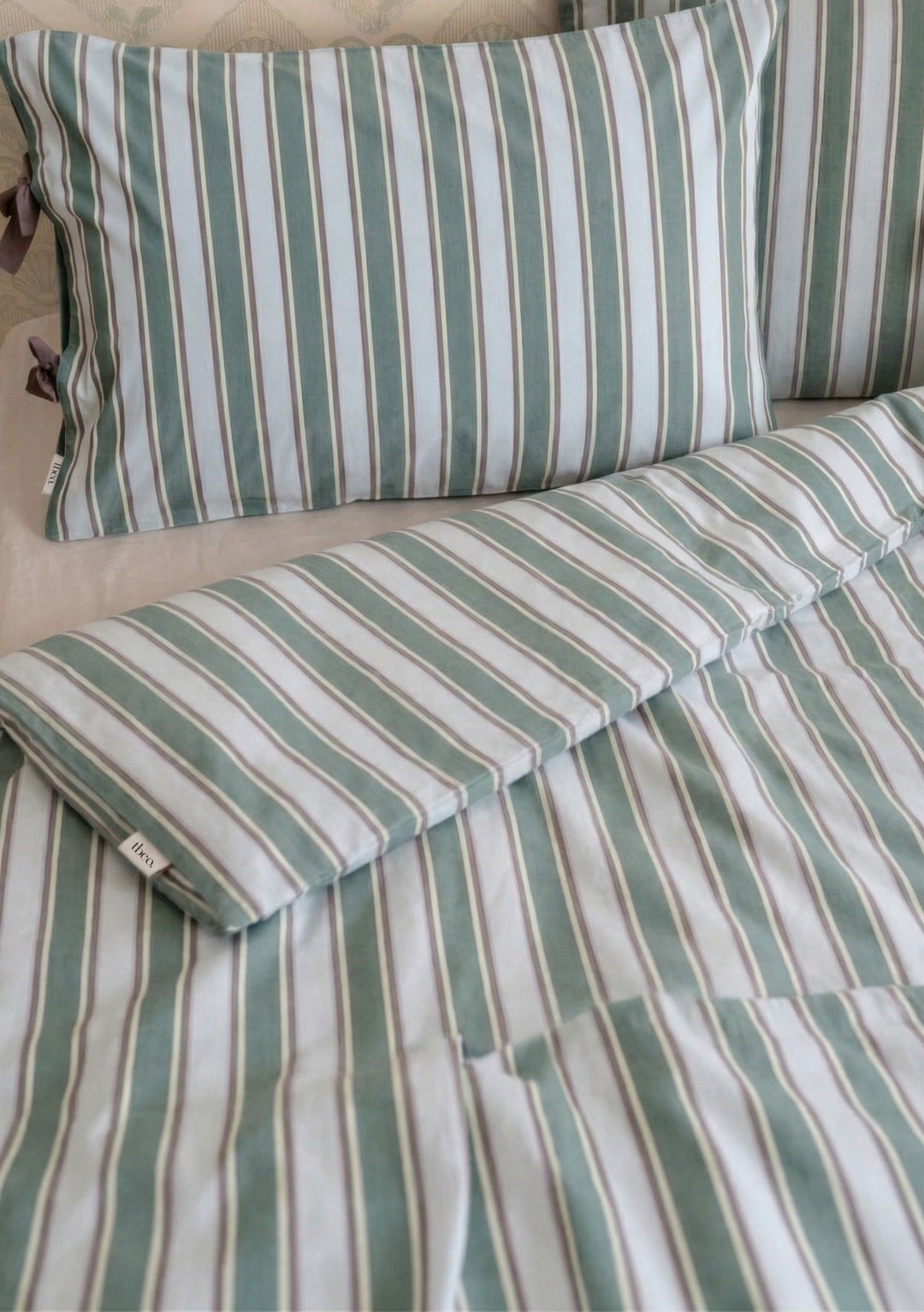 Pair of Cotton Pillowcases in Blue Stripe by TBCo featuring soft blue and white stripes with subtle brown bow ties on bed