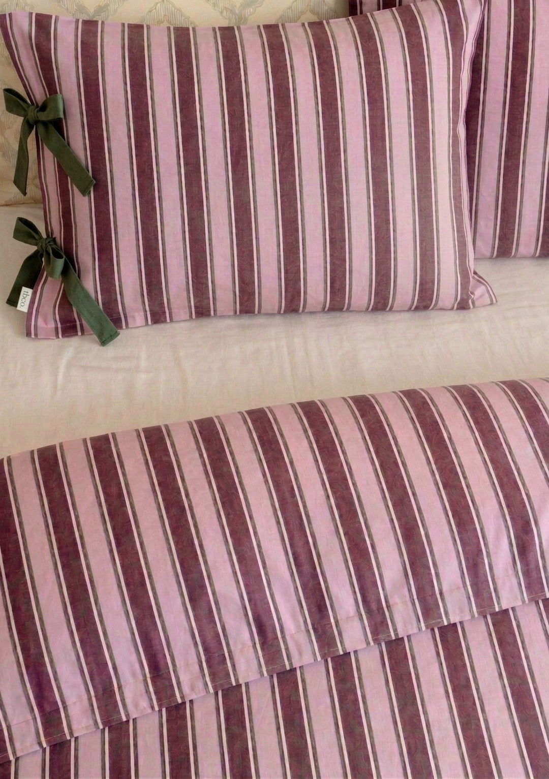 Pair of Cotton Pillowcases in Pink Stripe by TBCo with pink and burgundy vertical stripes and green bow accents on styled bedding