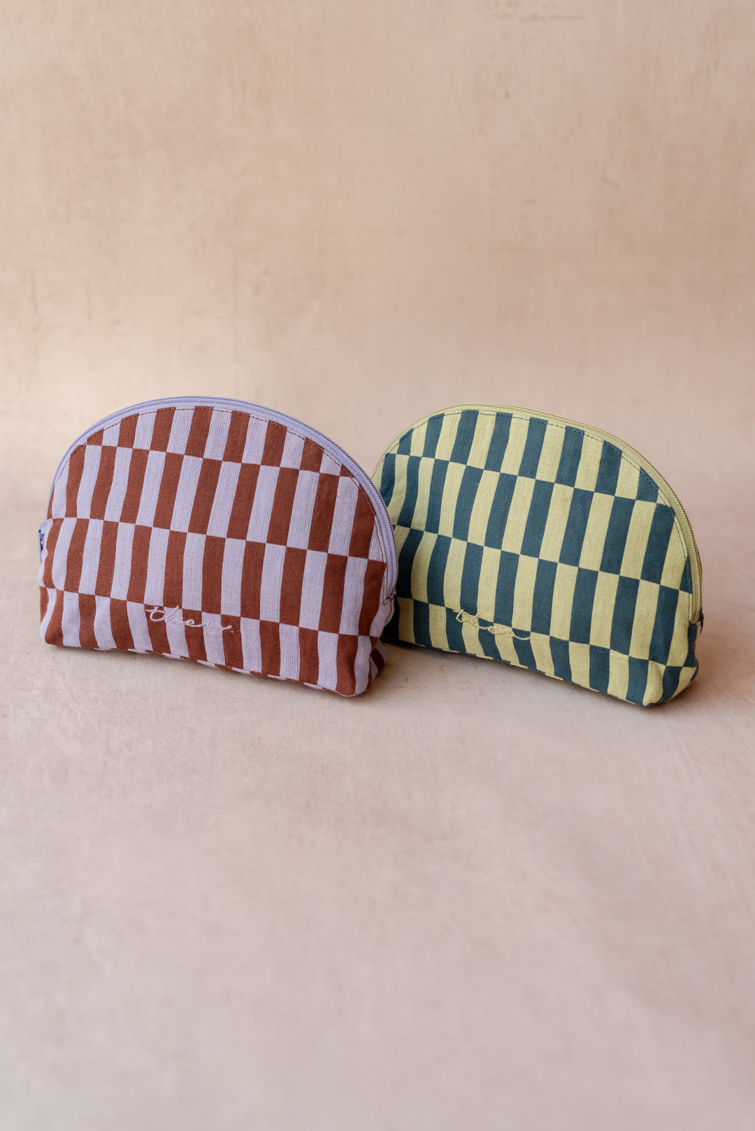 Two TBCo make-up pouches in checkerboard patterns sit against a neutral ply backdrop