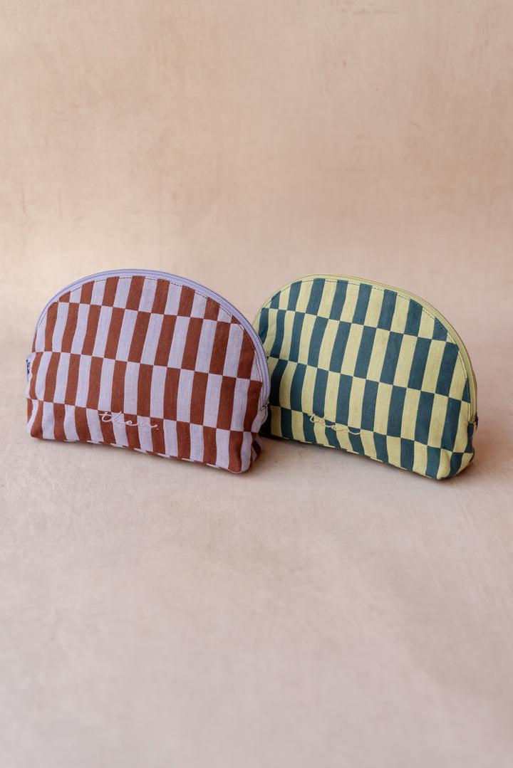 Two TBCo make-up pouches in checkerboard patterns sit against a neutral ply backdrop