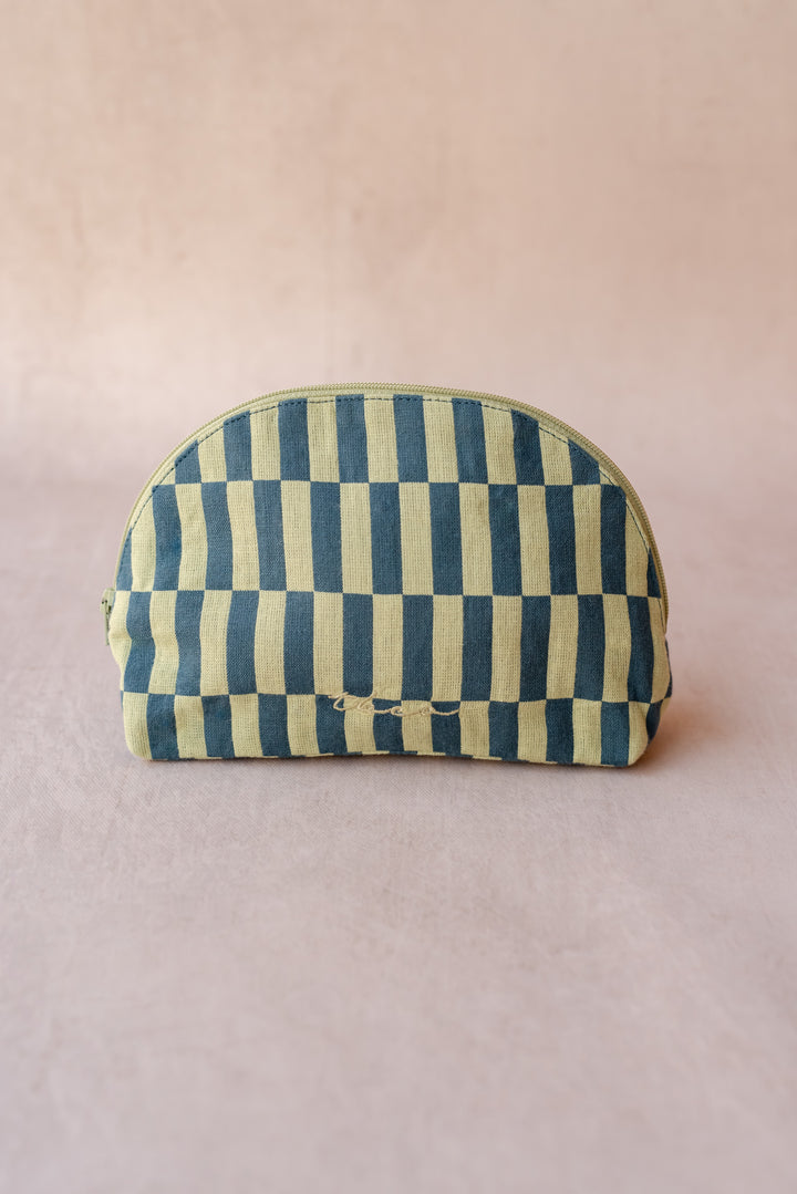 A TBCo make-up pouch in a green checkerboard pattern sits against a neutral ply backdrop