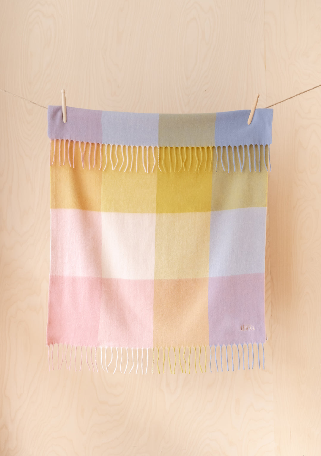 Lambswool Baby Blanket in Pink Block Check by TBCo hanging on a line with fringed edges in portrait view