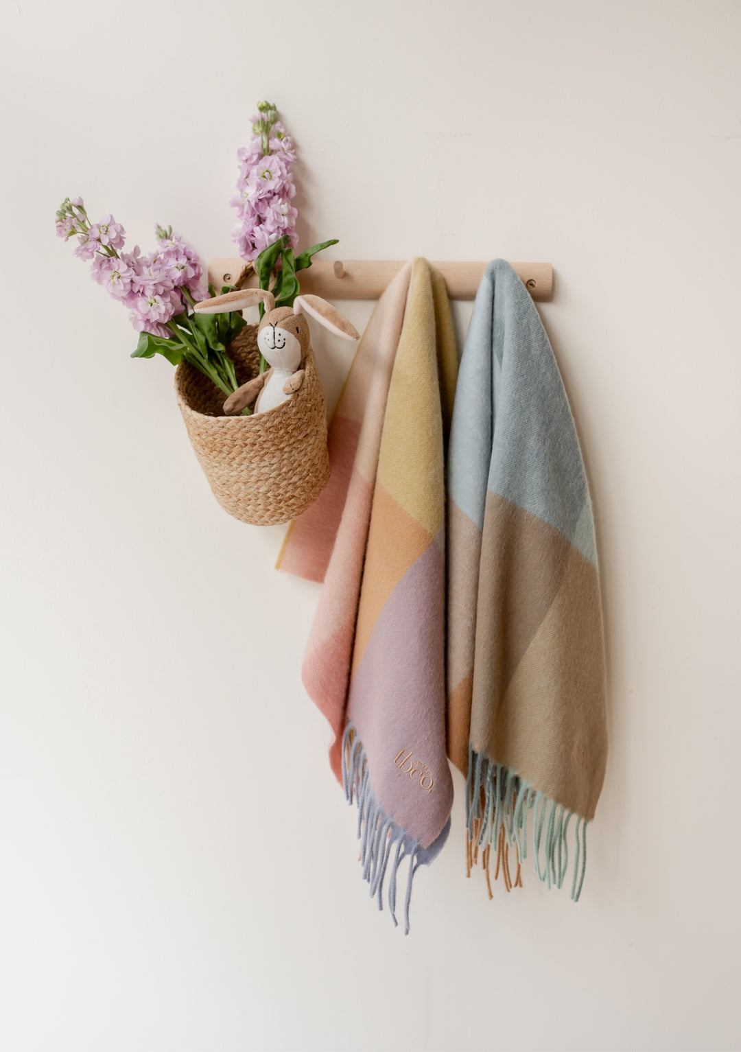 Lambswool Baby Blanket in Pink Block Check by TBCo hanging on wall with woven basket and soft toy portrait gallery shot