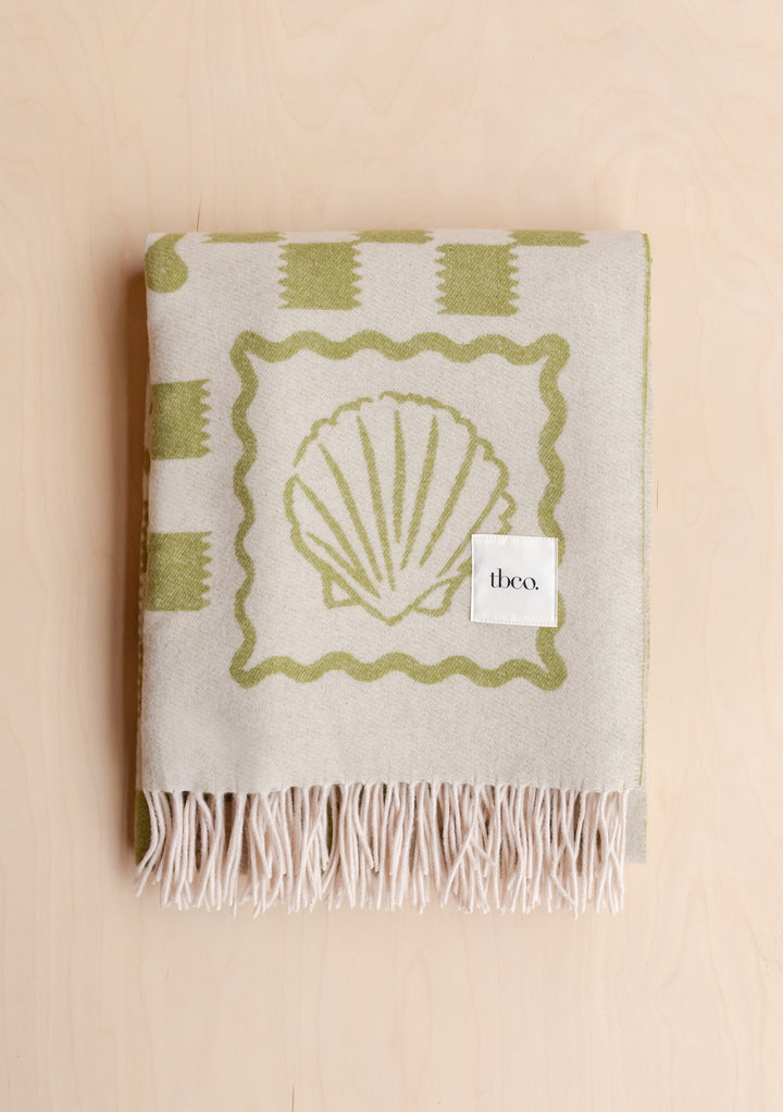 Folded TBCo Lambswool Blanket in Green Motif with fringed edges featuring olive green shell pattern, gallery position 4 portrait view