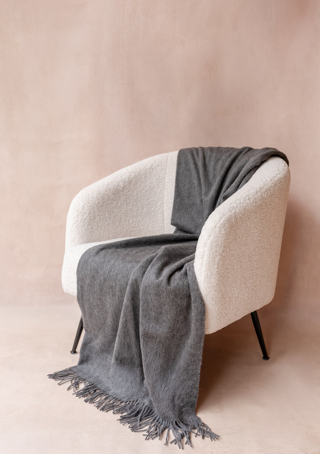 TBCo Cashmere Blanket in Charcoal Melange draped over a cream armchair showcasing soft fringed edges and luxurious texture